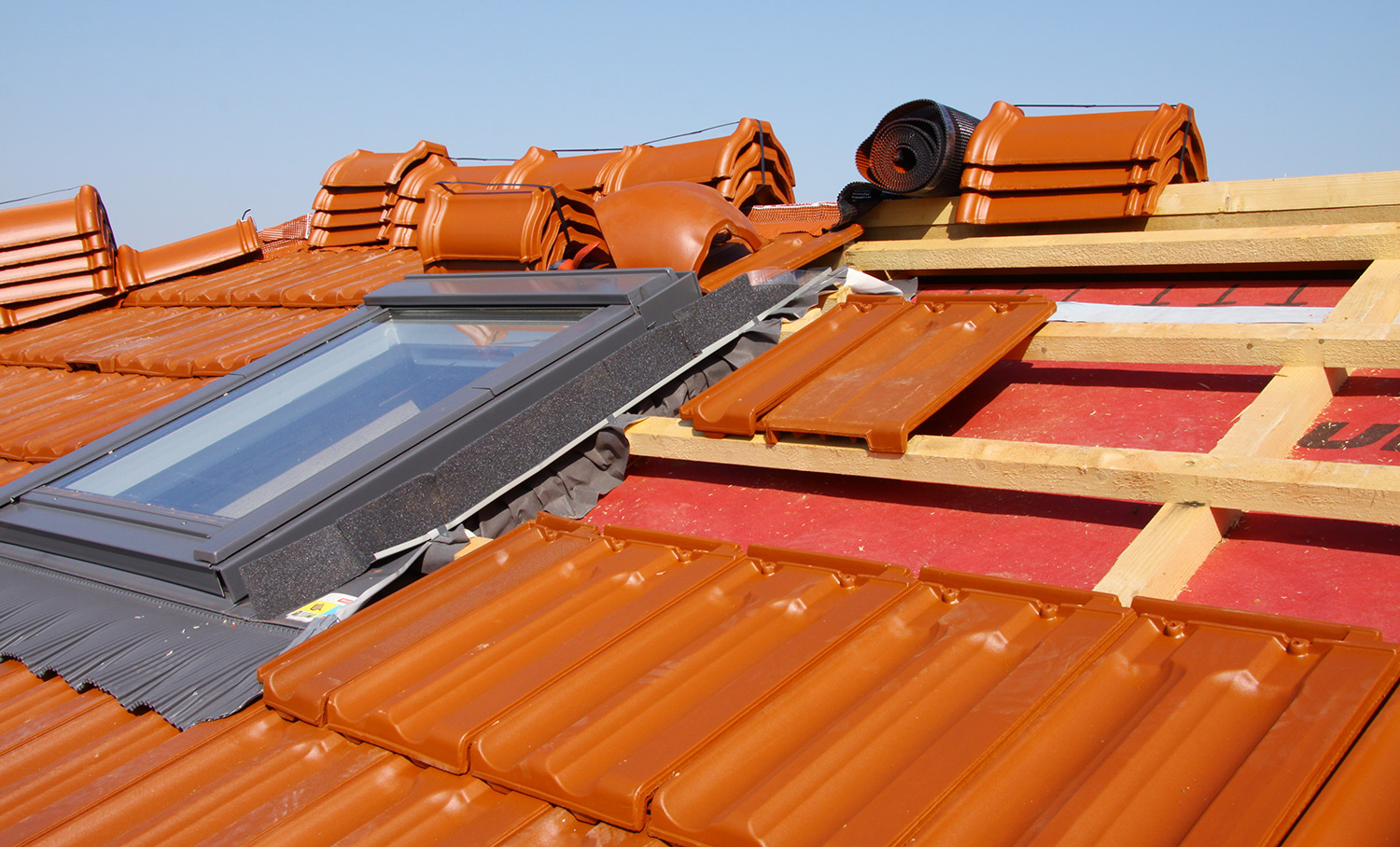 Dach mit roten Tonziegeln, teilweise verlegt, mit eingebautem Dachfenster und Holzlatten